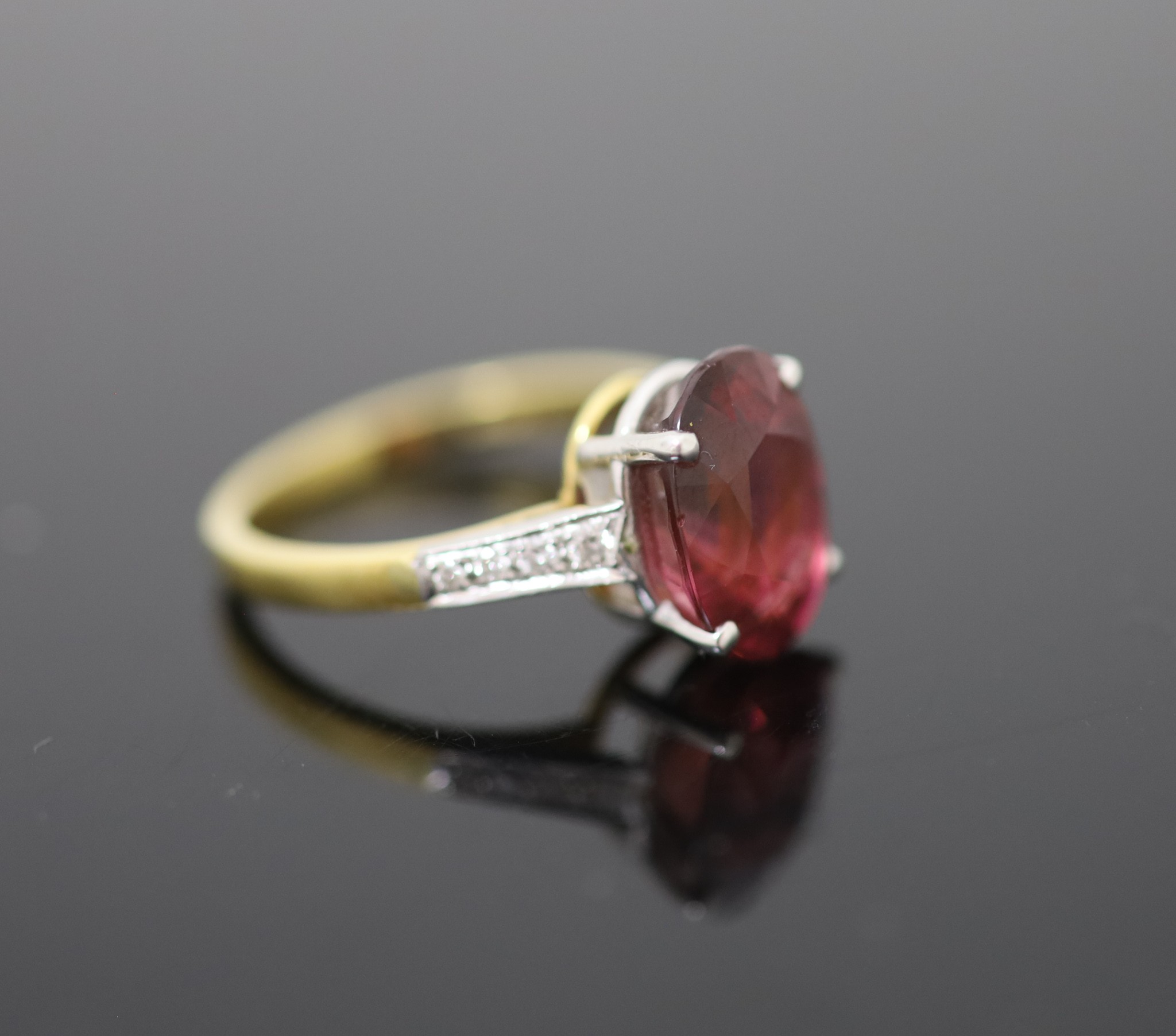 A modern 18ct gold and oval deep pink tourmaline ring, with diamond set shoulders